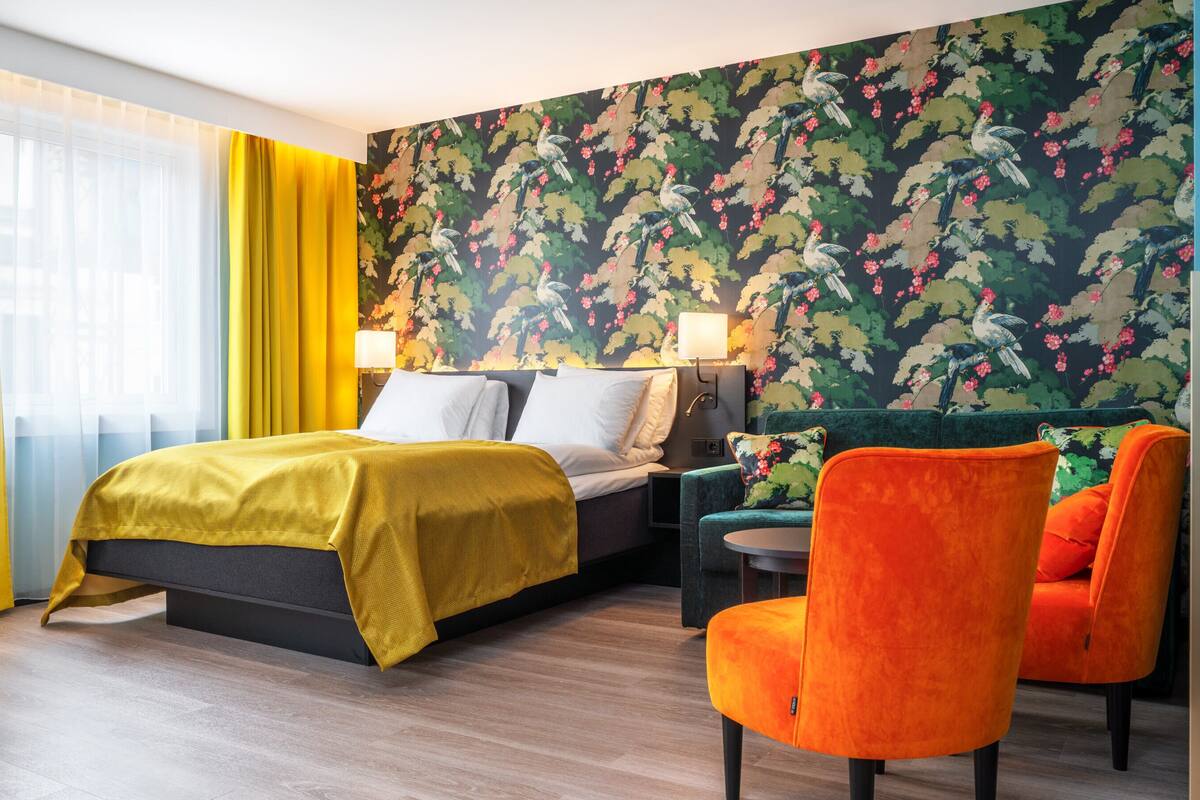 A hotel room with a bed, a desk, a chair, and a floral wallpaper.