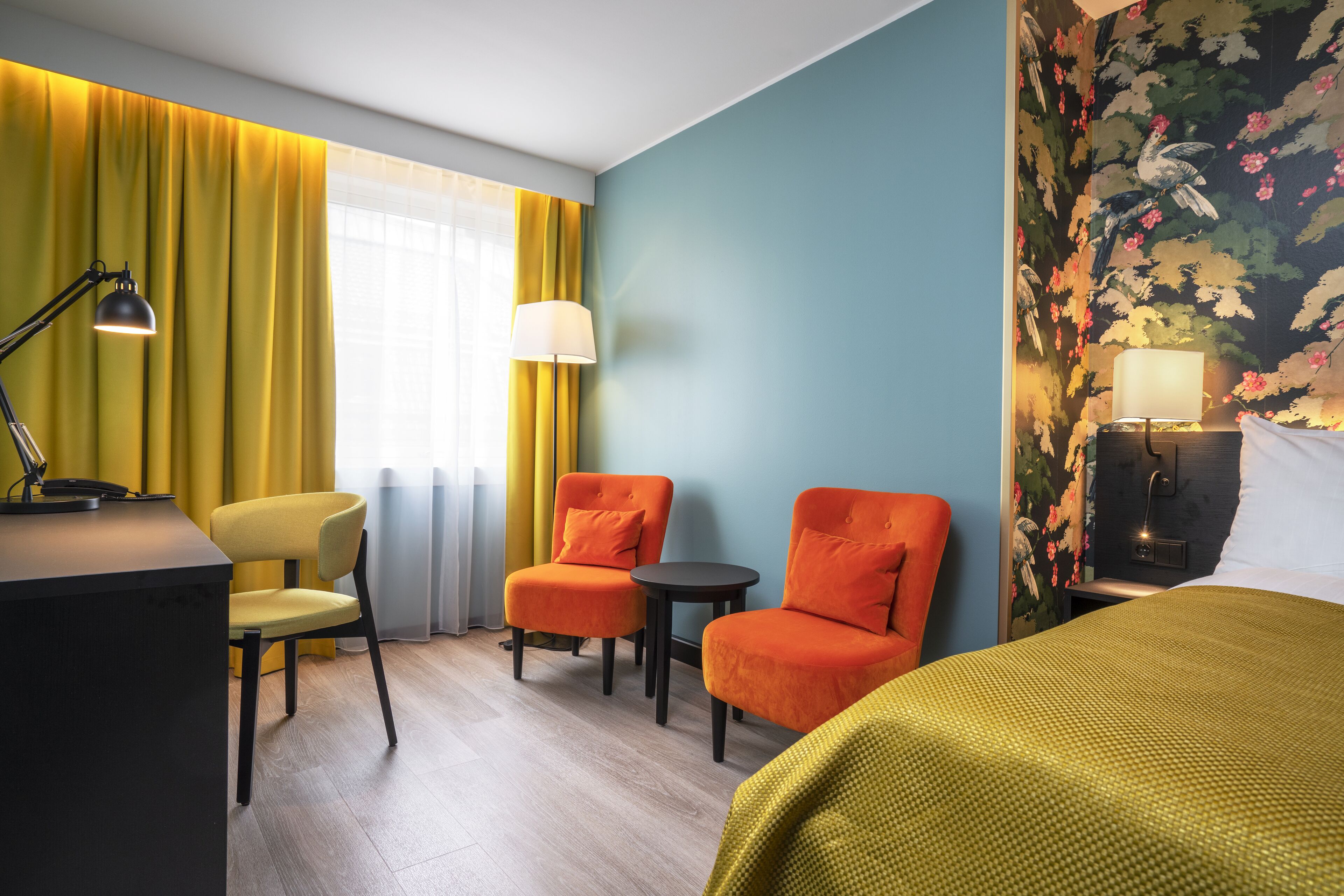 A hotel room with a bed, two armchairs, a desk, and a small table.