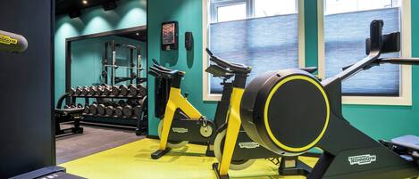 A gym with exercise equipment, a wall-mounted dumbbell rack, and a window with blinds.
