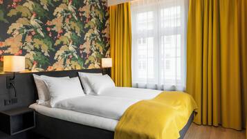 A hotel room with a bed, two bedside lamps, a nightstand, and a window with curtains.