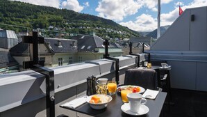 Terraza en la azotea con una mesa dispuesta para el desayuno, con vistas a un pueblo montañoso.