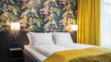 A hotel room with a bed, two bedside lamps, a nightstand, and a floral wallpaper.