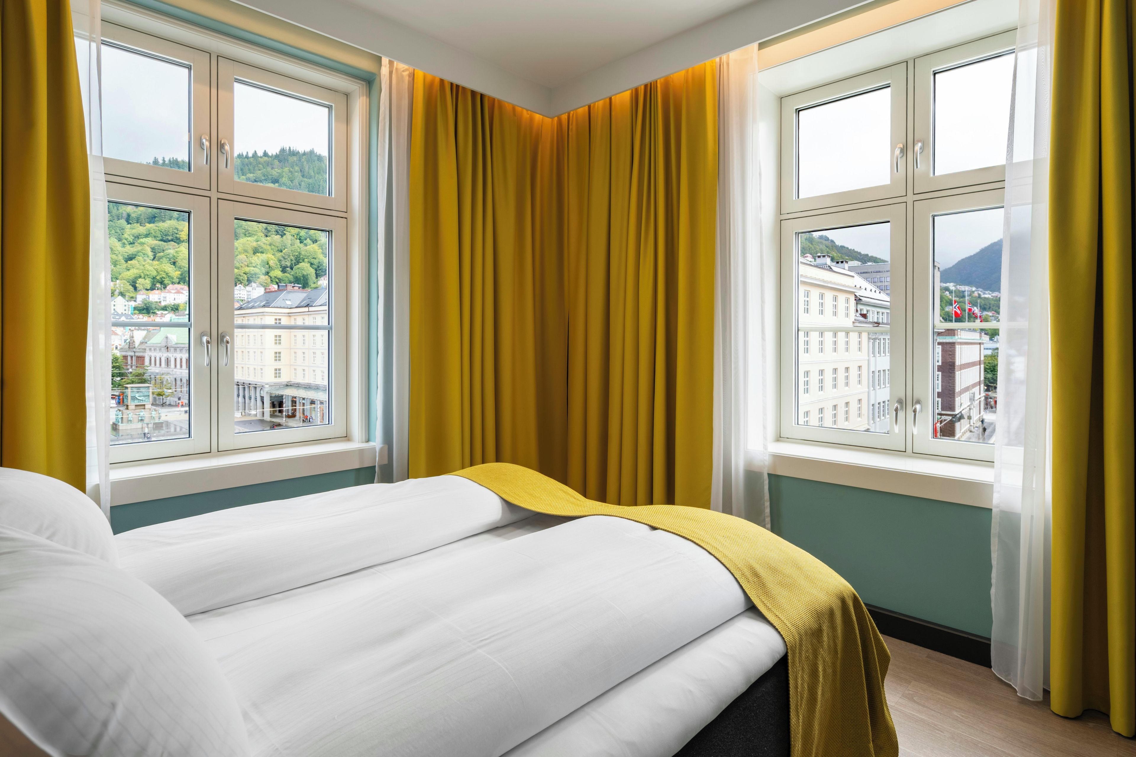 A hotel room with two beds, large windows, and curtains.