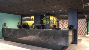Una zona de recepción con mostrador de mármol, una planta en maceta y un papel tapiz decorativo.