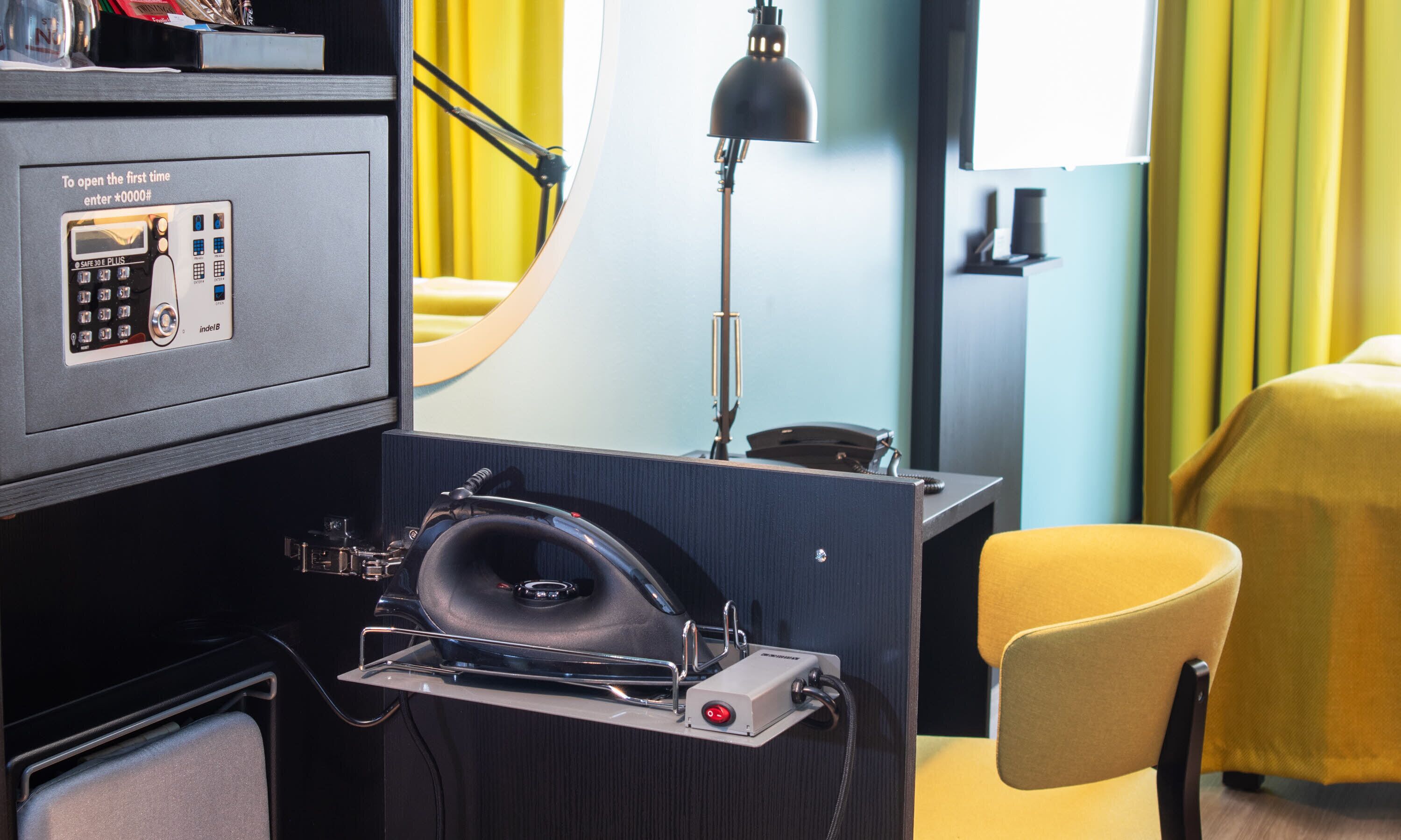 Ein Hotelzimmer mit Schreibtisch, Telefon, Safe, Soundsystem und einem gelben Stuhl.
