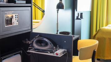 Ein Hotelzimmer mit Schreibtisch, Telefon, Safe, Soundsystem und einem gelben Stuhl.