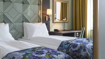 A hotel room with two beds, a desk, a lamp, and a mirror.