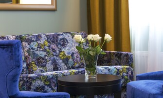 Una habitación con un sofá azul, una mesa redonda negra y un jarrón con flores blancas.