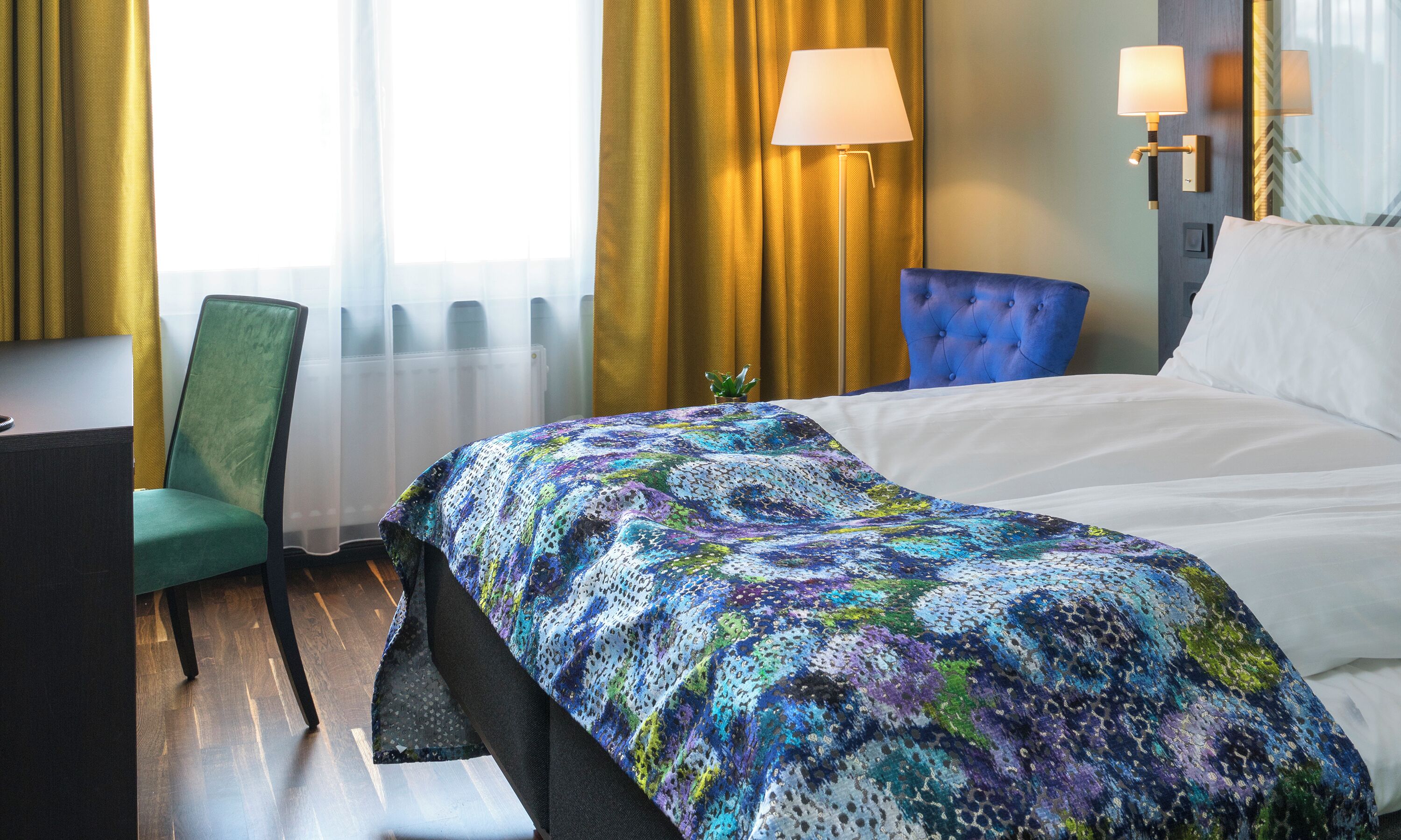 Een hotelkamer met een bed, een stoel, een bureau en een lamp.