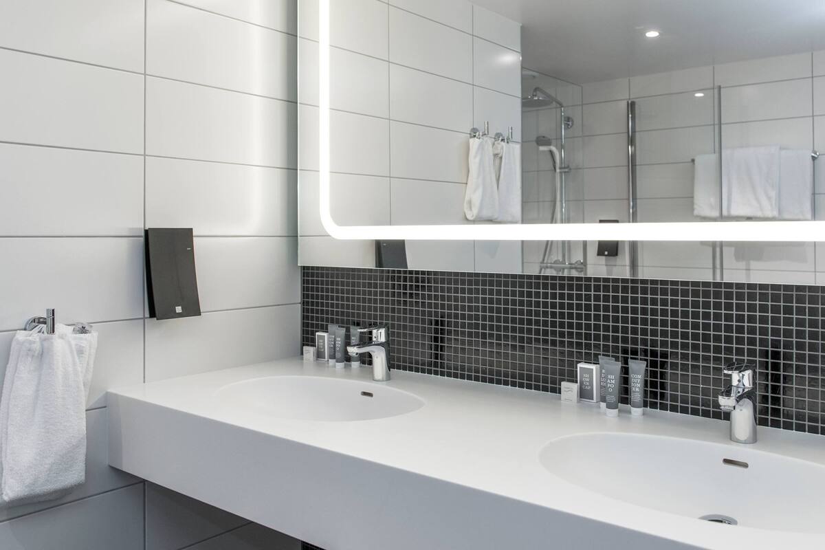 A modern bathroom with two sinks, a large mirror, and a shower.