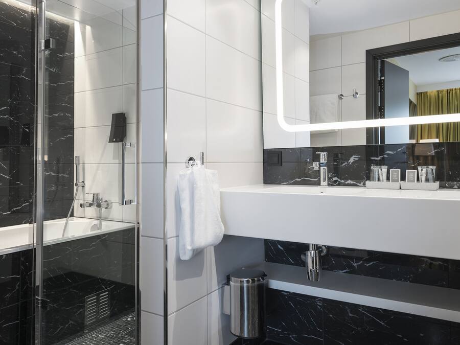 Un baño moderno con ducha envuelta en vidrio, un tocador blanco con salpicadero de mármol negro y un espejo grande con iluminación integrada.