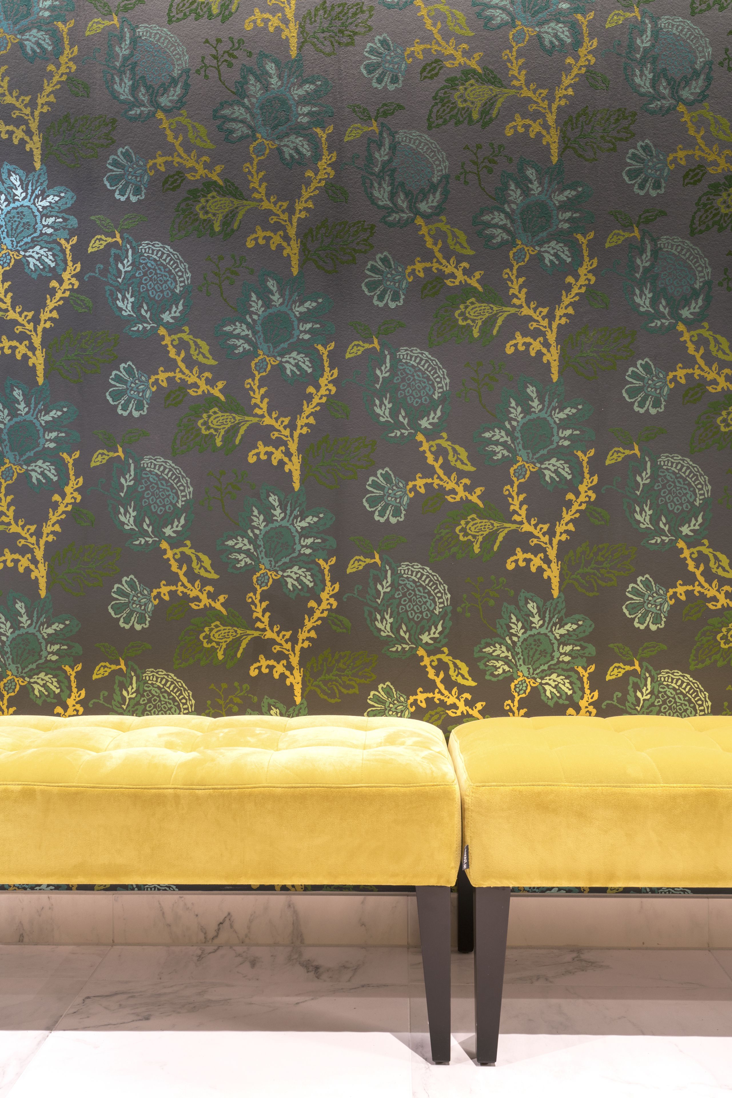 Una habitación con papel tapiz estampado con motivos florales y dos bancos tapizados en amarillo.