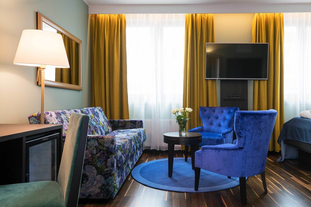 A hotel room with a sofa, armchair, TV, and a bed.
