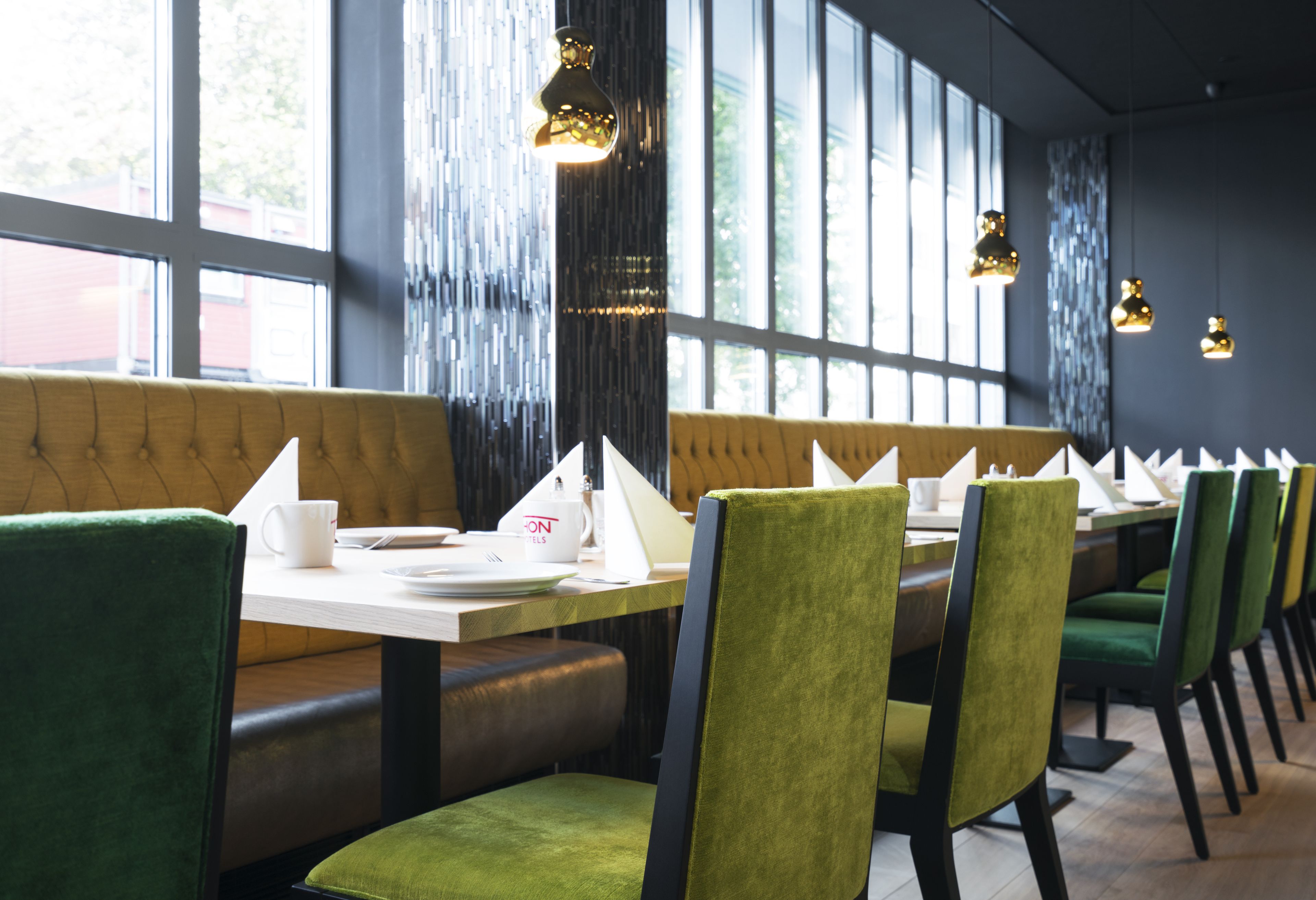 A restaurant with green upholstered chairs, a wooden bench, and a table set with white napkins and a coffee cup.