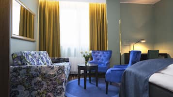 A hotel room with a sofa, two armchairs, a small table, a lamp, and a window with curtains.