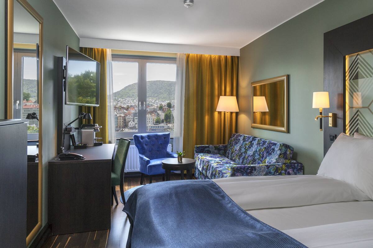 A hotel room with a bed, a desk, a chair, a table, and a view of the city.