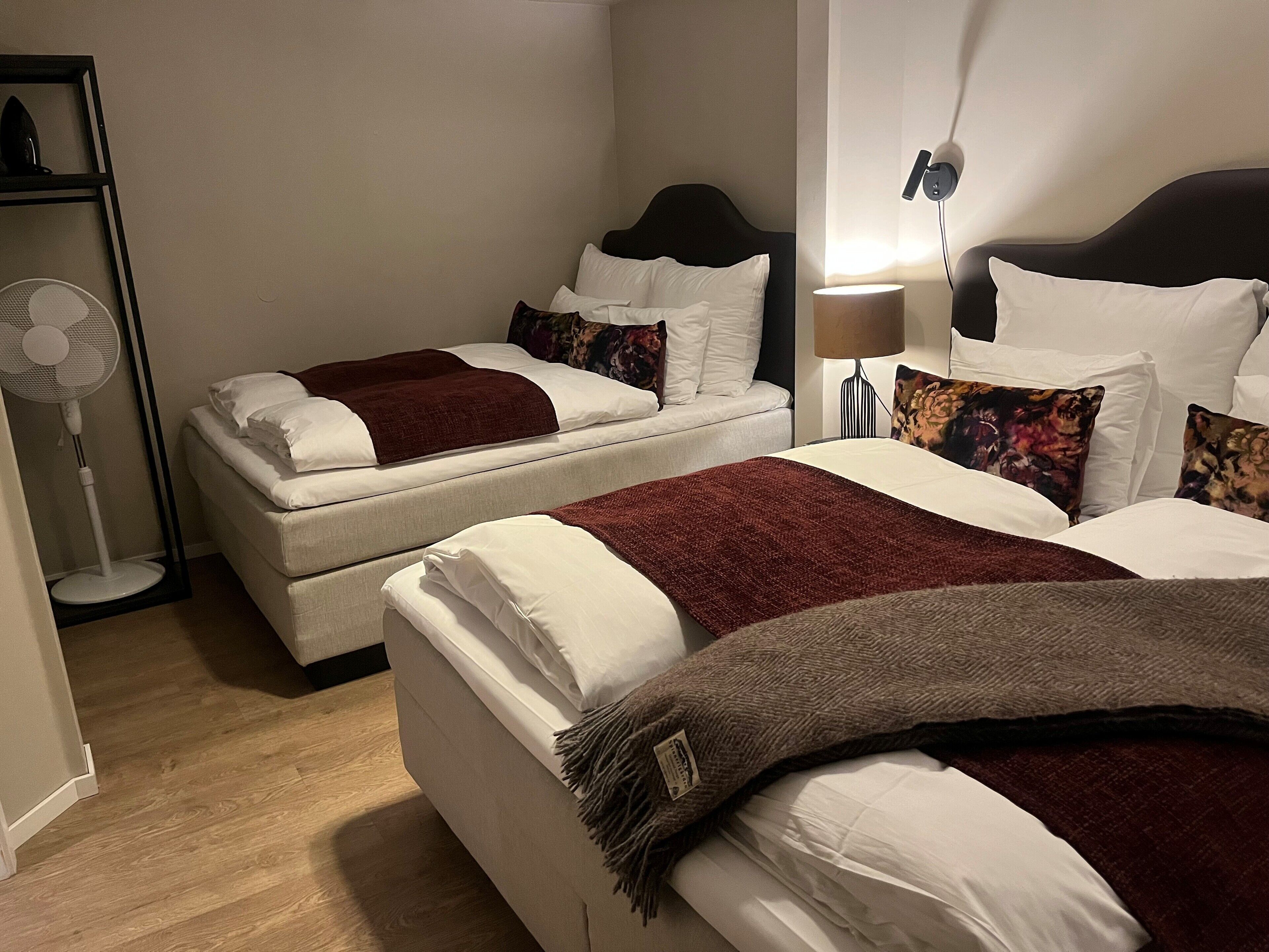 Une chambre d’hôtel avec deux lits, un ventilateur sur pied et une table de chevet avec une lampe.