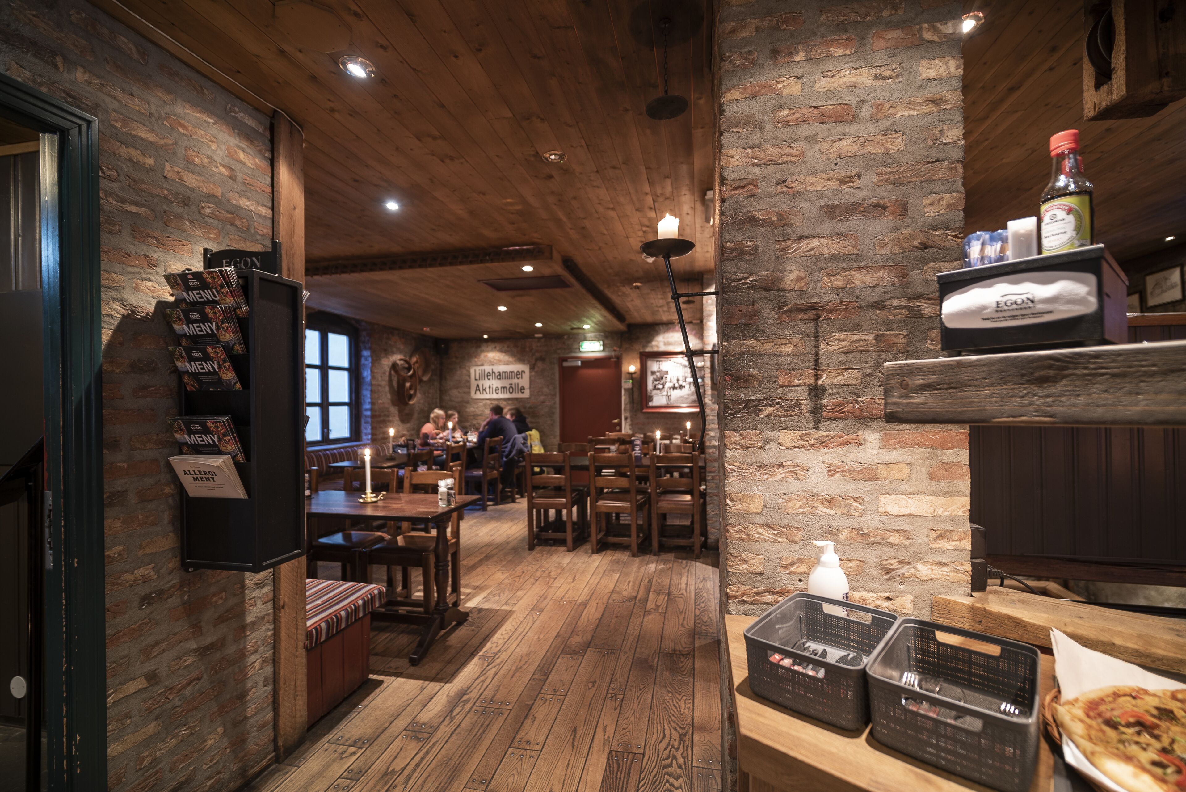 Interior de un restaurante con pisos de madera, paredes de ladrillo y un atril para el menú.