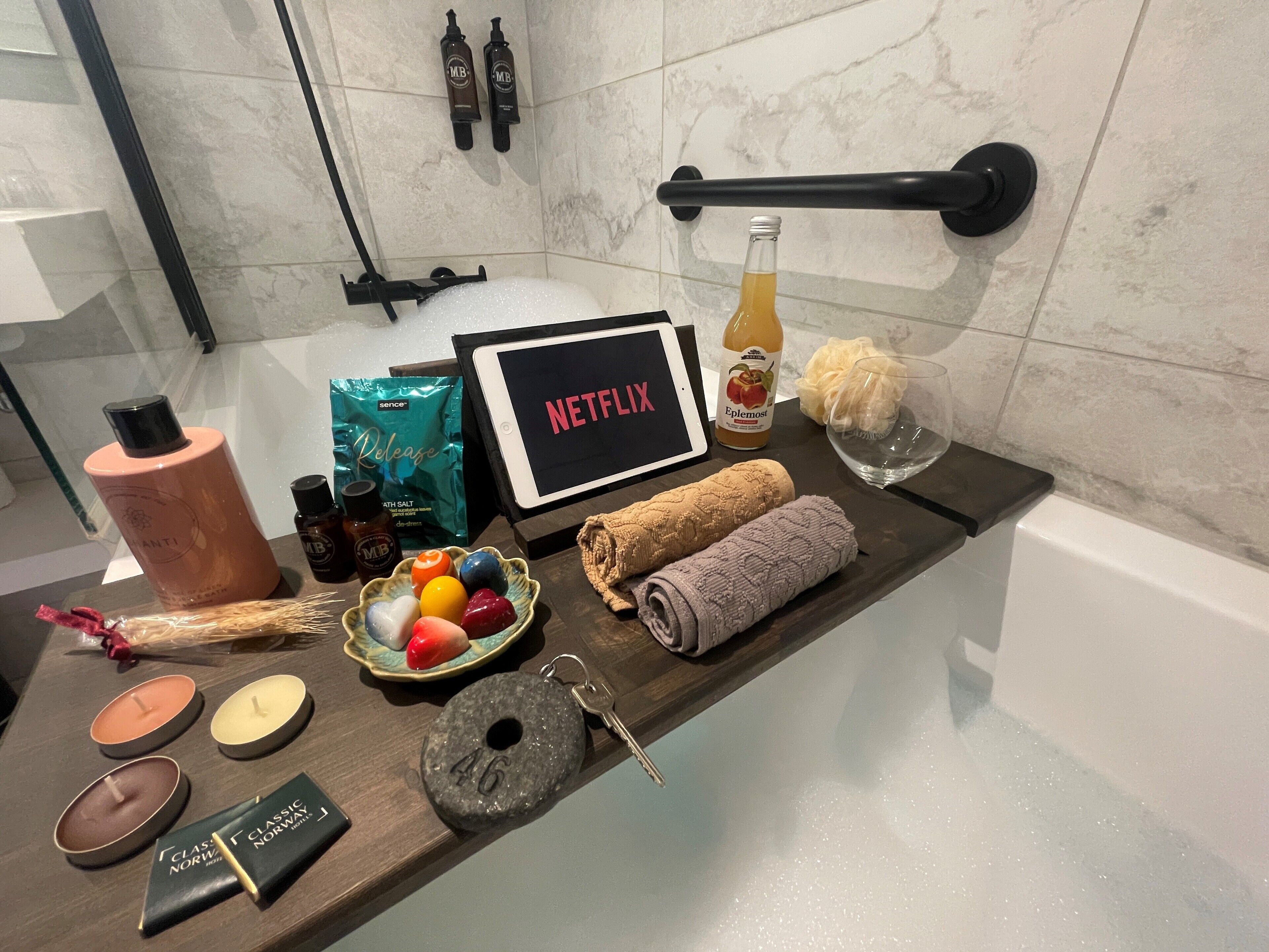 Un tocador de baño con artículos de aseo, un cartel de Netflix, una bomba de baño, una botella de Ephemerol, una esponja de baño y una toalla.