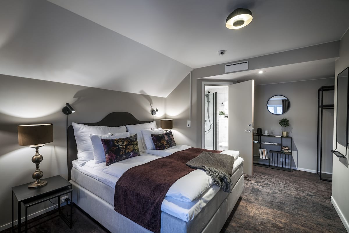 A modern bedroom with a large bed, bedside lamps, a dresser, and a mirror.