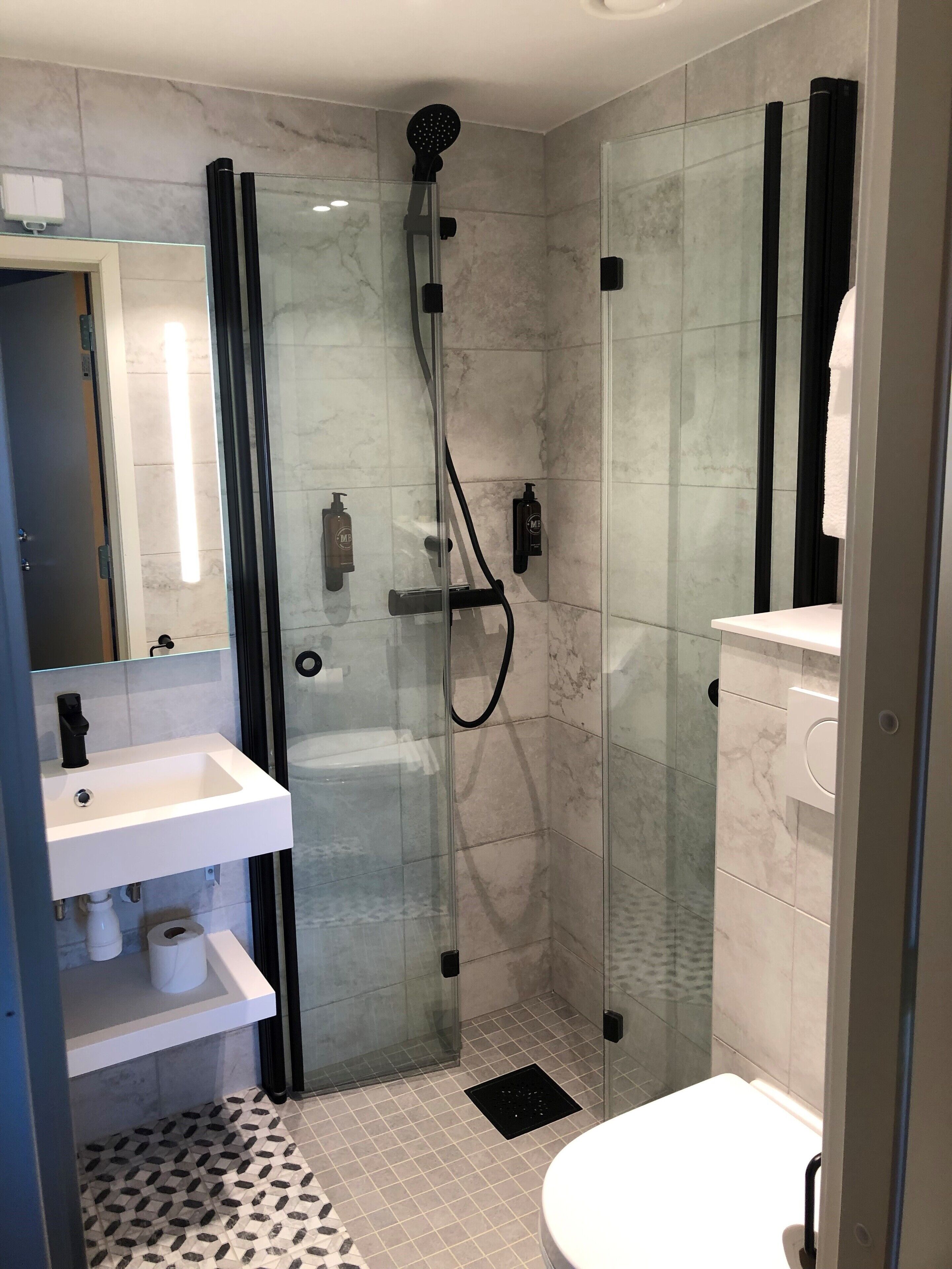 Et moderne badeværelse med en glasafskærmet brusekabine, en hvid vask og et toilet.