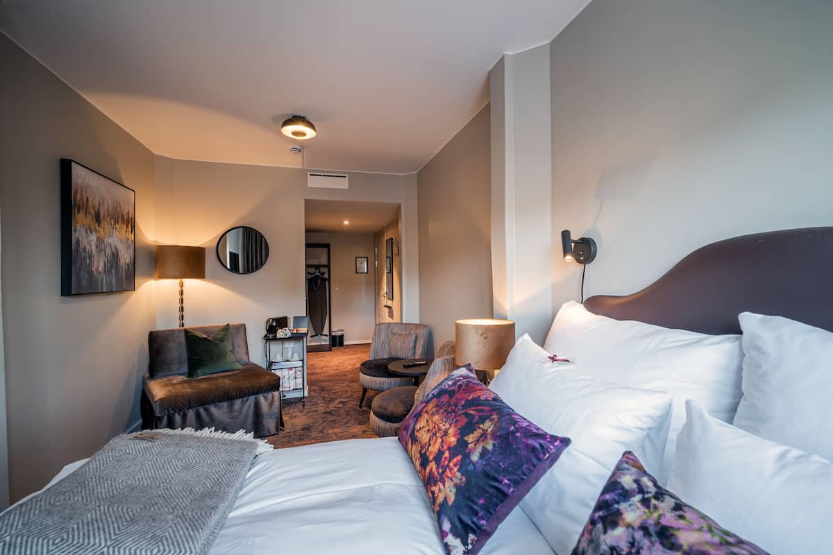 A hotel room with a bed, a chair, a desk, and a lamp.