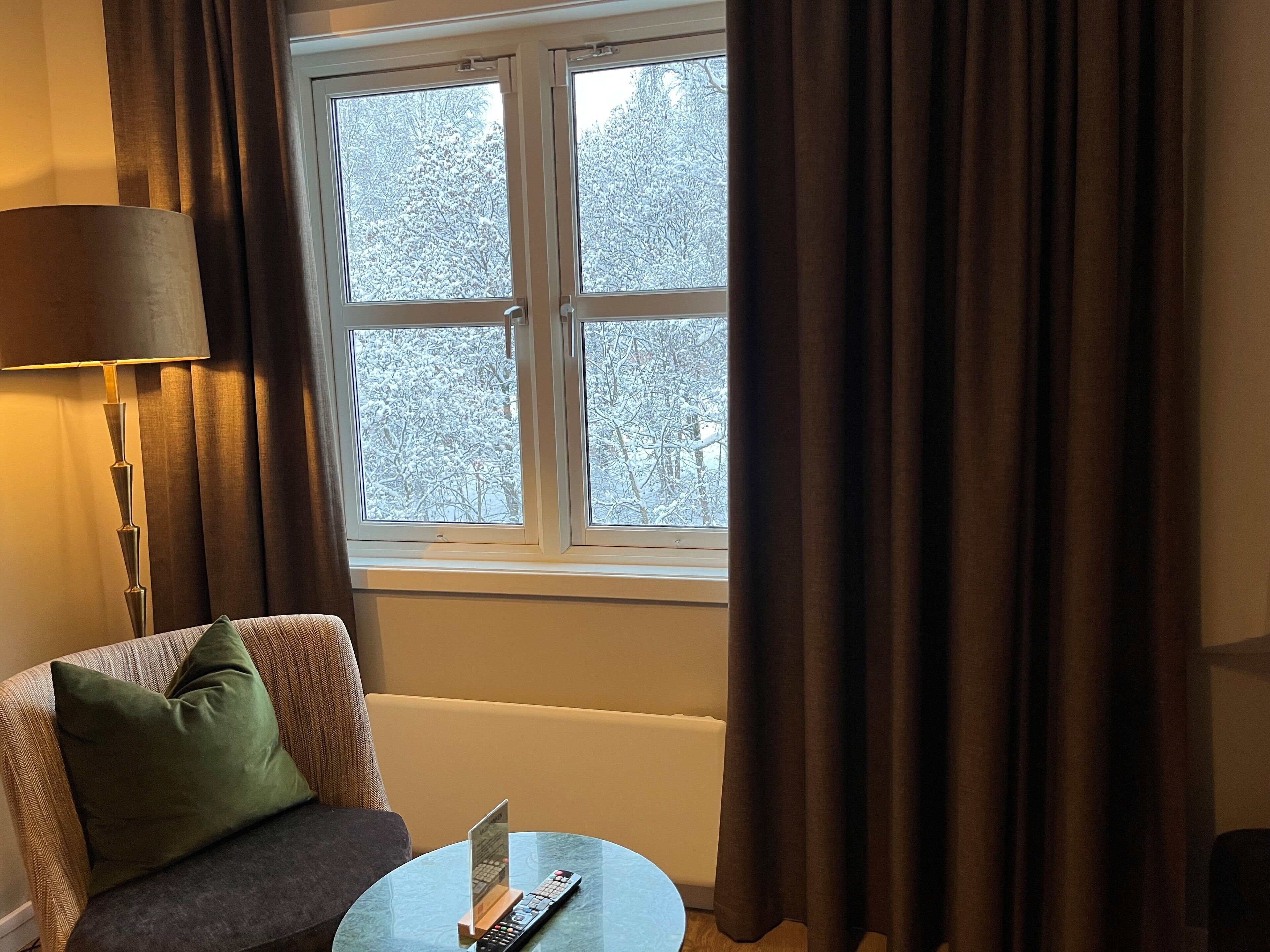 Una habitación con un sofá, una mesa con un control remoto y una ventana con cortinas.