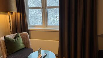 Una habitación con un sofá, una mesa con un control remoto y una ventana con cortinas.