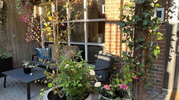 Un patio con pared de ladrillo, una ventana, un sofá con cojines y plantas en macetas.
