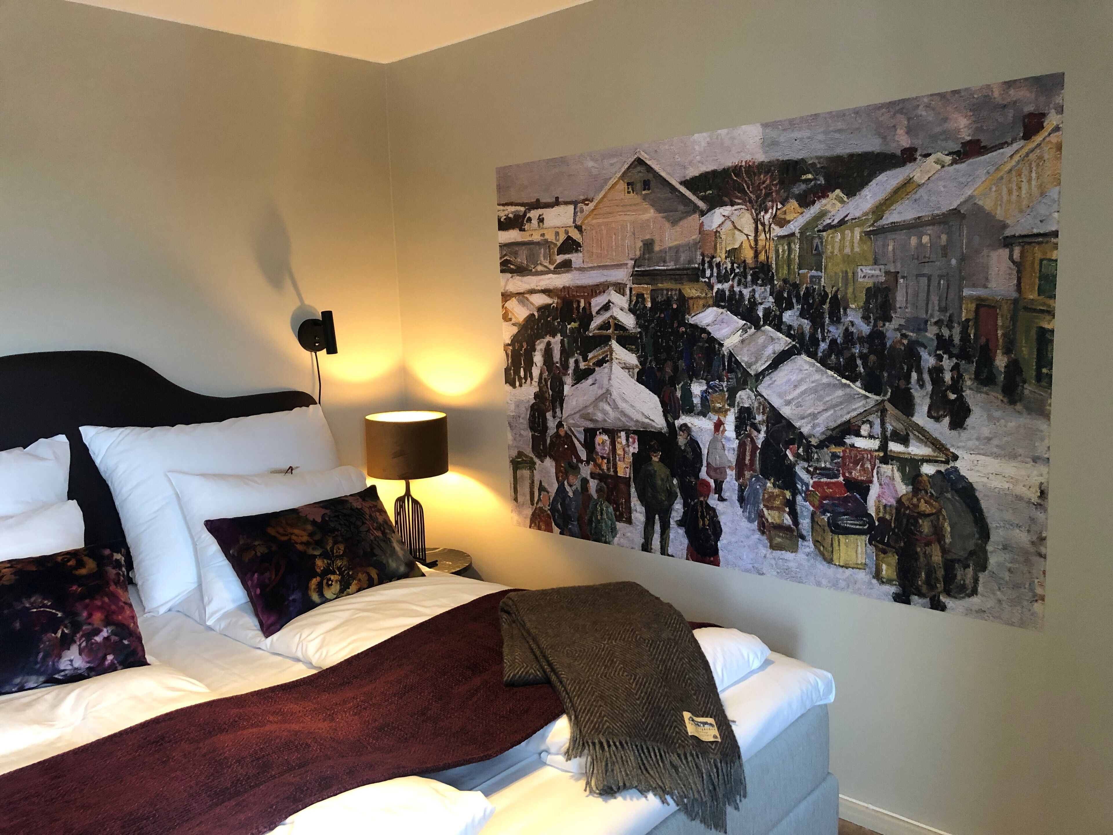 A hotel room with a bed, a lamp, and a large winter-themed painting on the wall.