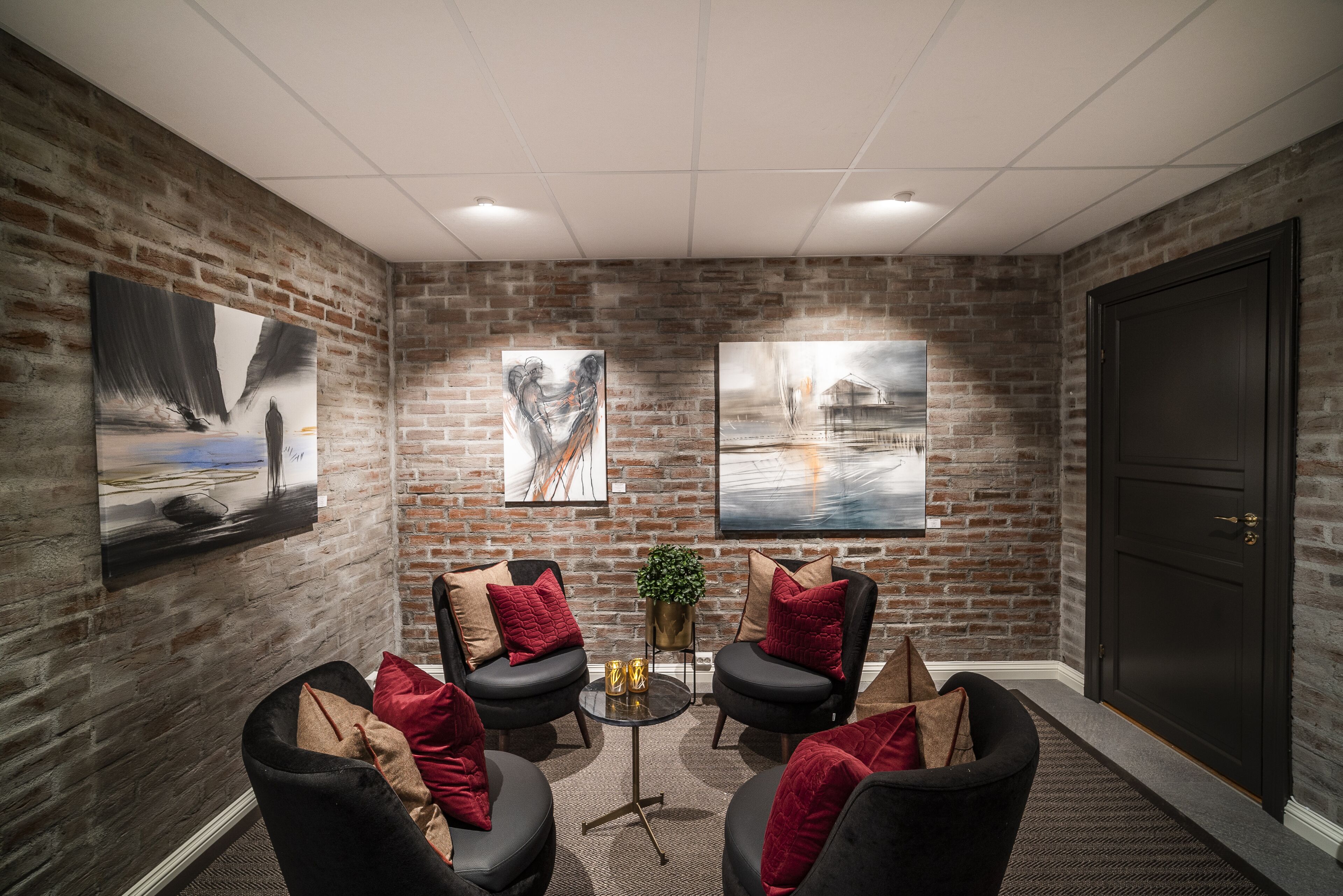 A conference room with brick walls, black leather chairs, red cushions, and two paintings.