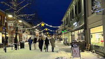 Una calle nevada con comercios y un árbol de Navidad decorado con luces.