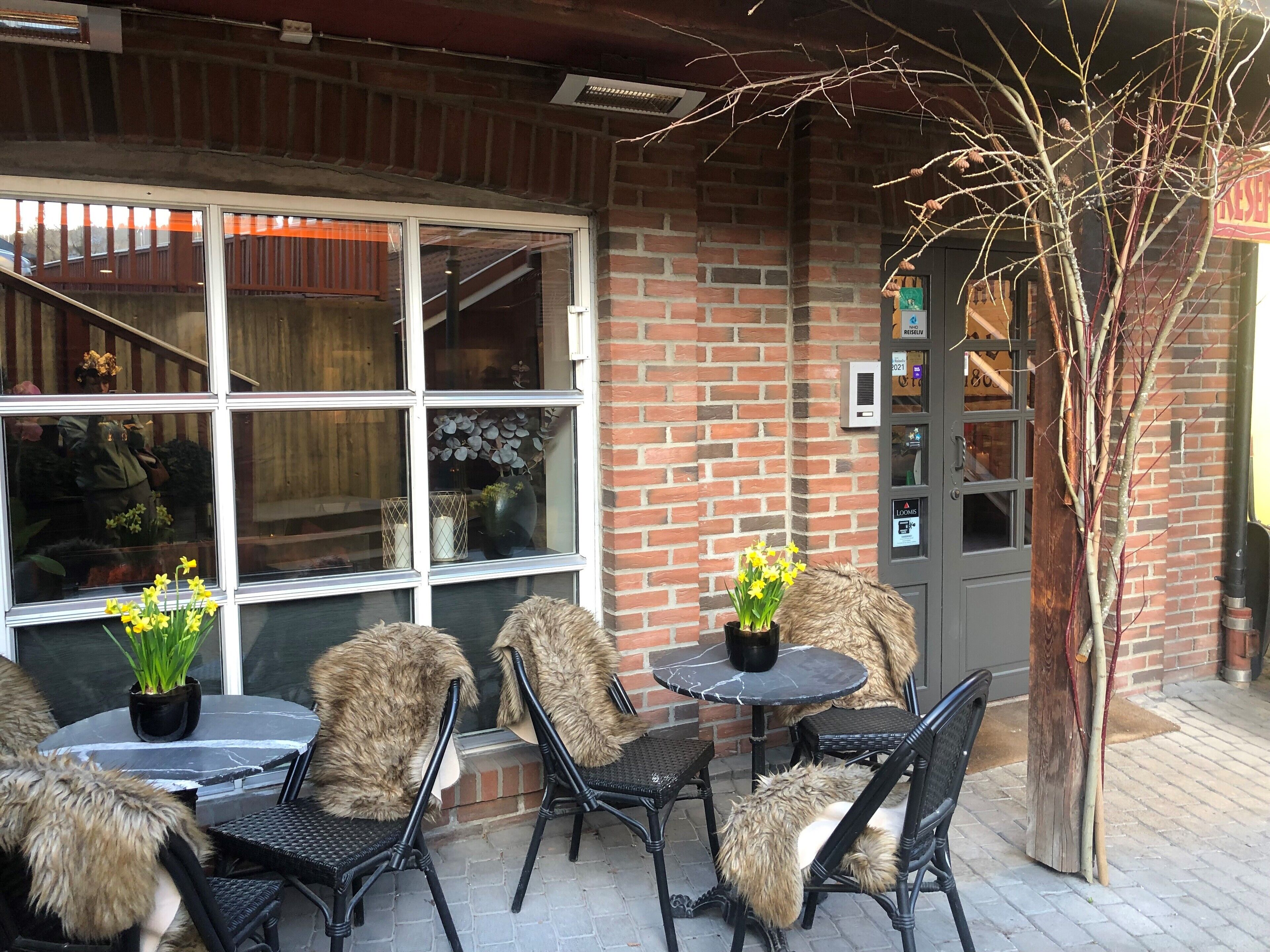 An outdoor seating area with brick walls, a glass door entrance, and a small tree.
