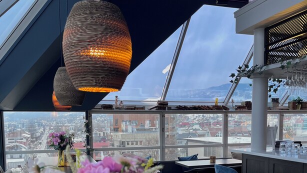 A modern bar area with a city view, a large vase of flowers, and hanging pendant lights. - Aksjemøllen - by Classic Norway Hotels (Lillehammer)