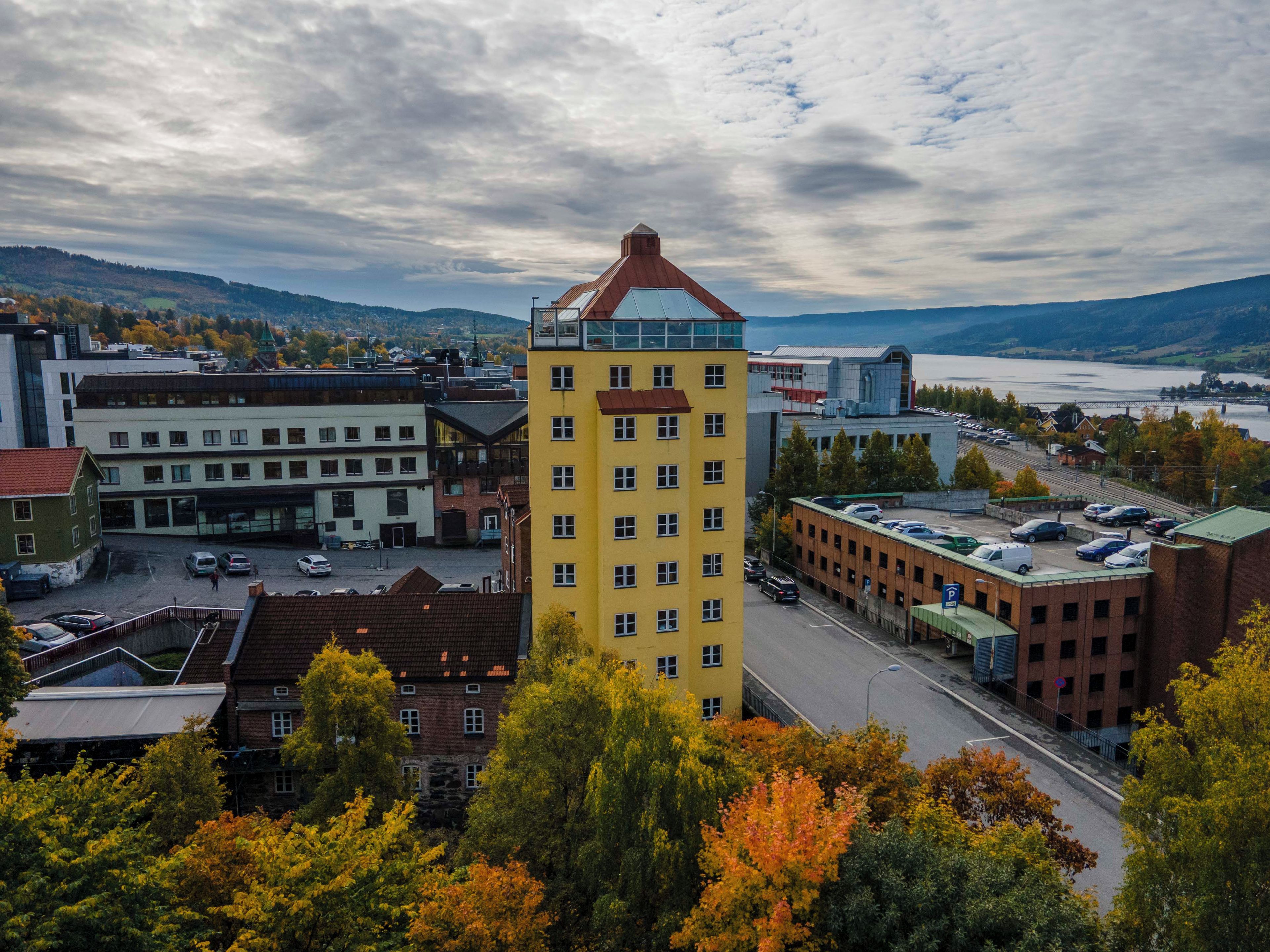 A multi-story building with a prominent yellow facade and a red roof, surrounded by other buildings and a parking lot.