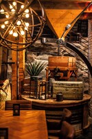 Un interior rústico con una mesa de madera, sillas, una lámpara globo y una maleta antigua.