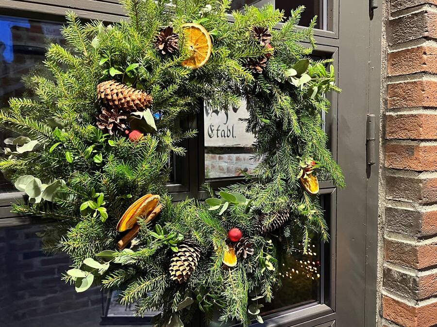A wreath with pine cones, dried orange slices, and a sign that reads "Stab."