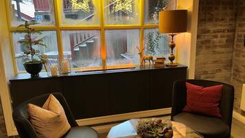 Una zona de estar acogedora con dos sillones, una mesita con una planta y una ventana con luces decorativas.