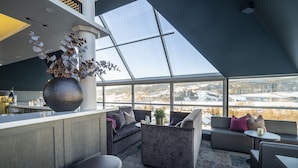 A modern interior with a high ceiling, a skylight, a bar area, and a seating arrangement with a view of a snowy landscape. - Aksjemøllen - by Classic Norway Hotels (Lillehammer)