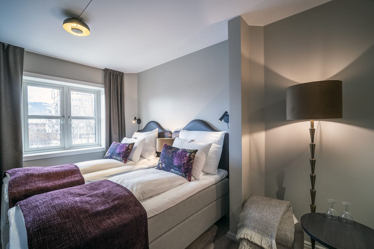 A hotel room with two beds, a window, a lamp, and a small table.