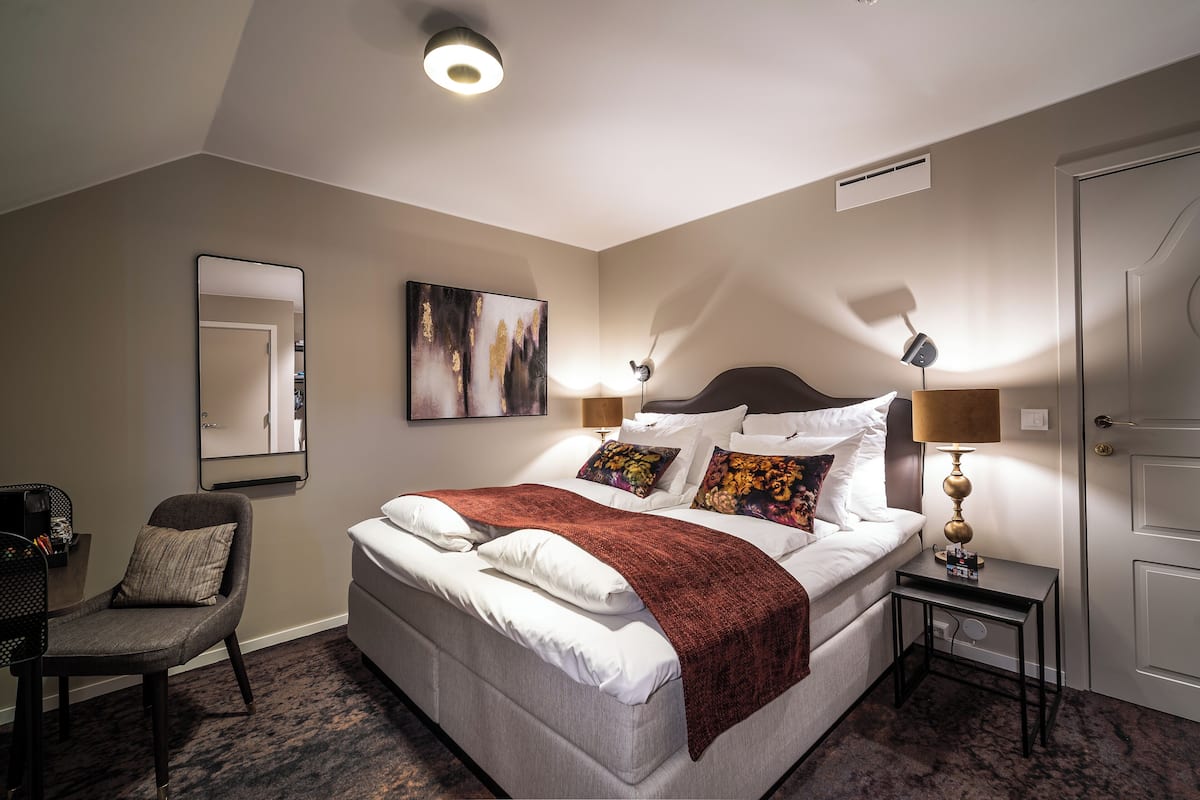 A hotel room with a bed, a chair, a desk, and a lamp.