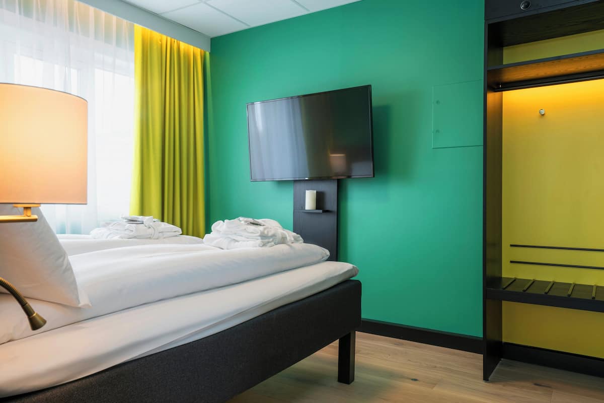 A hotel room with a bed, a television mounted on the wall, and a yellow door.