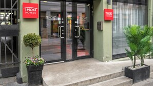 A hotel entrance with a red sign, a small tree, and a potted plant.
