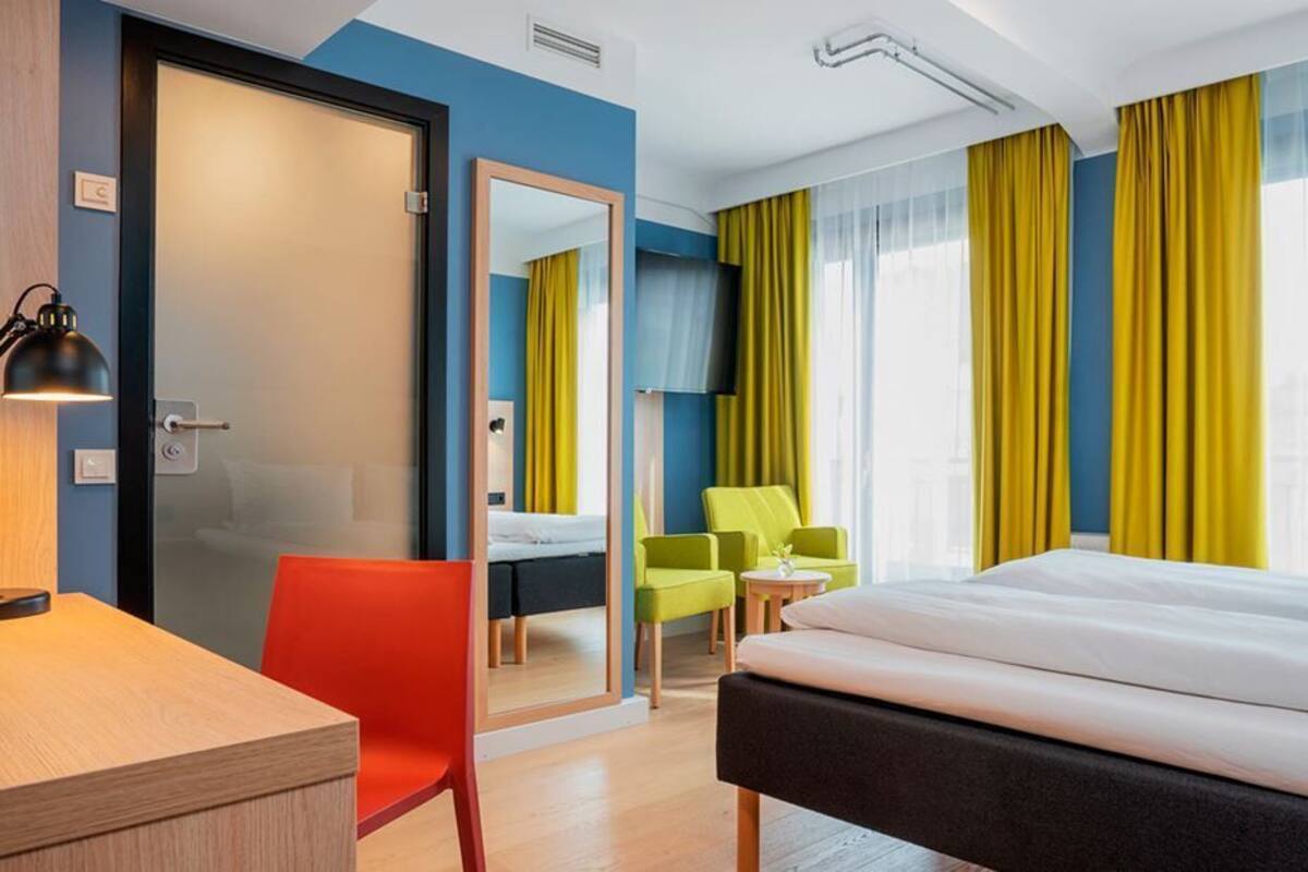 Une chambre d’hôtel avec un lit, un bureau, une chaise et un miroir.