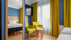 A hotel room with a bed, a desk, two chairs, a small table, and a TV.