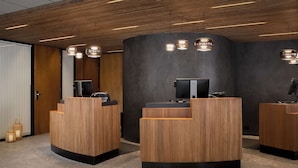 A reception area with wooden reception desks, a large mirror, and pendant lighting. - Scandic Victoria (Oslo)