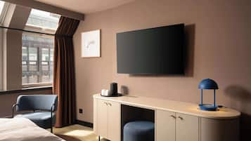 Et hotelværelse med en seng, to stole, et skrivebord med lampe, et fladskærms-tv og et vindue med gardiner.