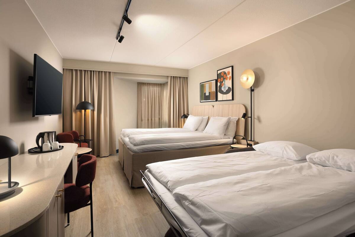 Una habitación de hotel con dos camas, un escritorio con lámpara, televisor y cafetera.