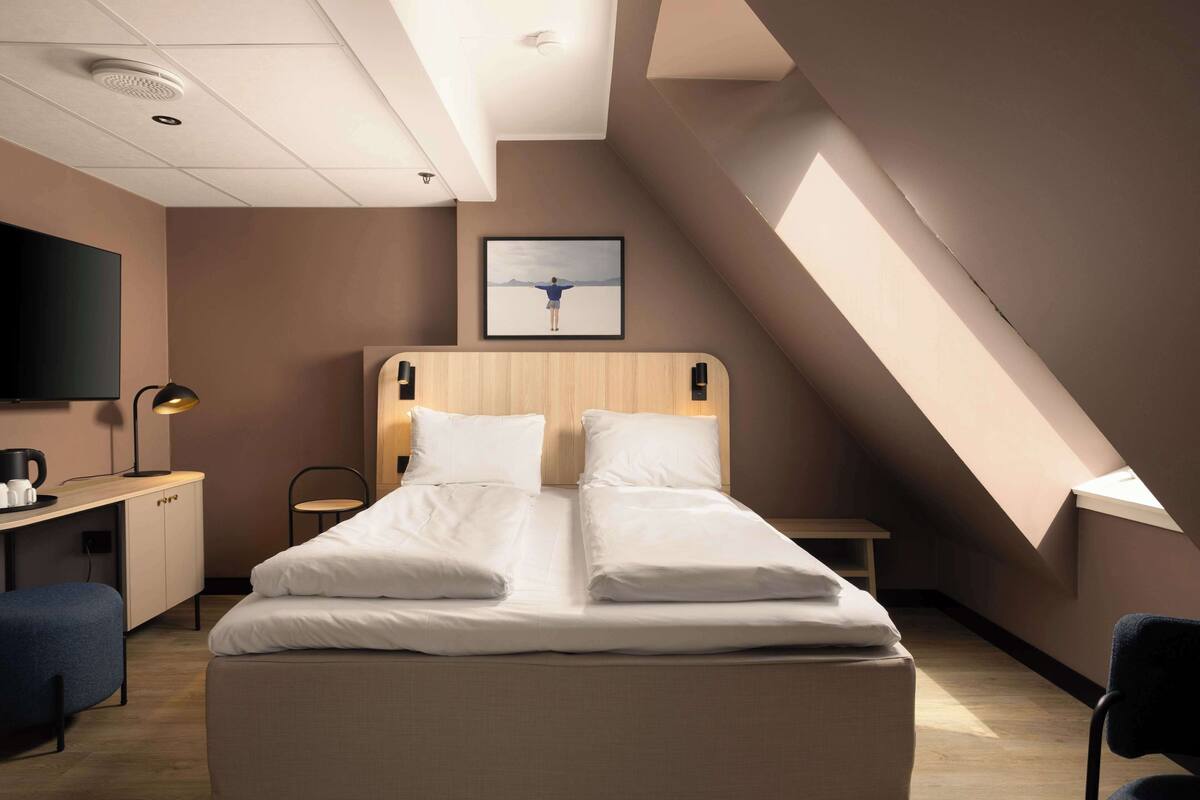 Un hotel moderno con una cama grande, un escritorio con silla, un televisor de pantalla plana y un cuadro en la pared.
