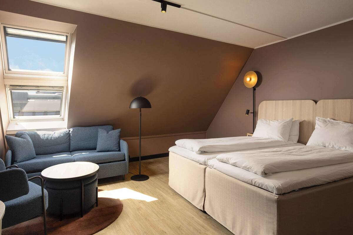 Un dormitorio moderno con un sofá, dos camas, una mesa redonda y una lámpara de pie.